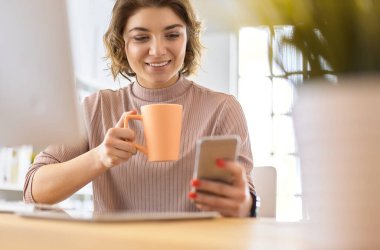 Genç iş kadını, ofiste dizüstü bilgisayarın önünde otururken mesaj atıyor.