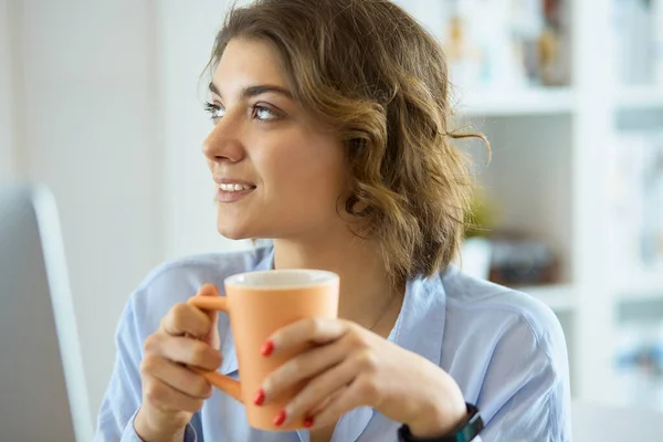 Attractive woman sitting at office desk, holding a cup of coffee — Stock Photo, Image