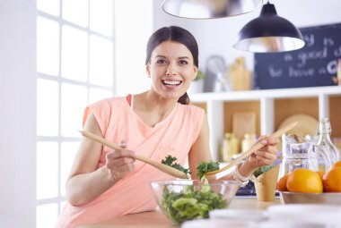 Gülümseyen genç kadın mutfakta taze salata karıştırıyor..