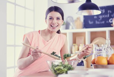 Gülümseyen genç kadın mutfakta taze salata karıştırıyor..