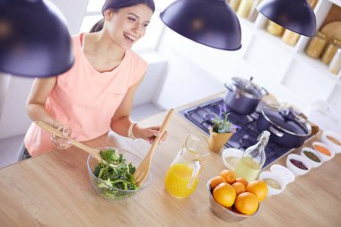 Gülümseyen genç kadın mutfakta taze salata karıştırıyor..