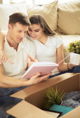 Yeni evlerinde karton kutuları açan sevimli bir çift yerde oturuyor ve bir aile albümüne bakıyor.