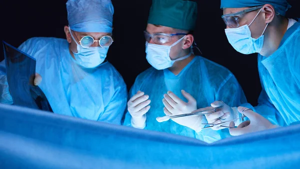 Grupo de cirurgiões no trabalho em sala de operações tonificada em azul. Equipe médica realizando operação — Fotografia de Stock