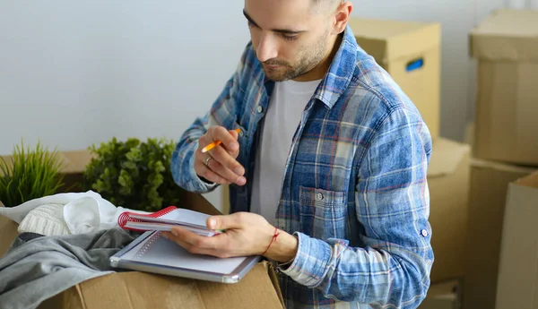 A moving man sitting on the floor in empty apartment, Among the Boxes, Checking the List of Things