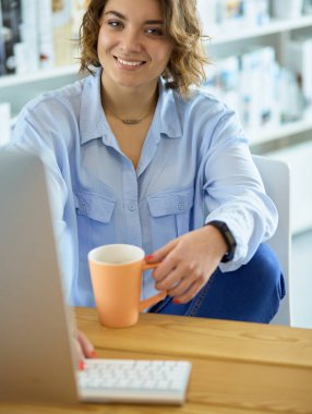 Ofis masasında oturan çekici bir kadın elinde bir fincan kahve tutuyor.