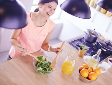 Gülümseyen genç kadın mutfakta taze salata karıştırıyor..