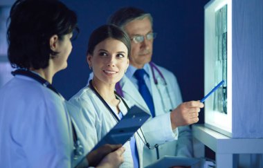 Bir grup doktor bir klinikte röntgenleri inceliyor, teşhis koymayı düşünüyorlar.