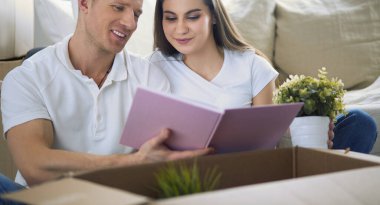 Yeni evlerinde karton kutuları açan sevimli bir çift yerde oturuyor ve bir aile albümüne bakıyor.