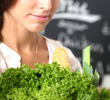 Mutfakta elinde sebzelerle gülümseyen genç bir kadın. Gülümseyen genç kadın