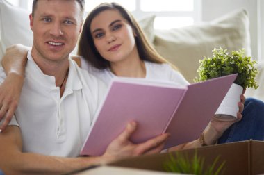 Yeni evlerinde karton kutuları açan sevimli bir çift yerde oturuyor ve bir aile albümüne bakıyor.