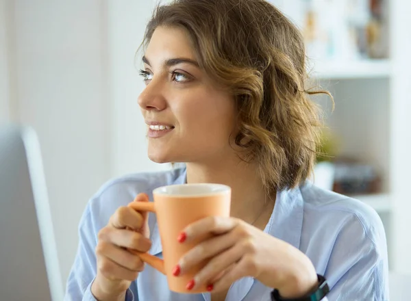 Attraktiv kvinna som sitter vid skrivbordet och håller en kopp kaffe — Stockfoto