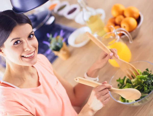 Mujer joven sonriente mezclando ensalada fresca en la cocina. —  Fotos de Stock
