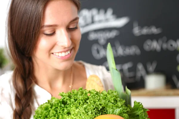 Wanita muda tersenyum memegang sayuran berdiri di dapur. Senyum wanita muda — Stok Foto