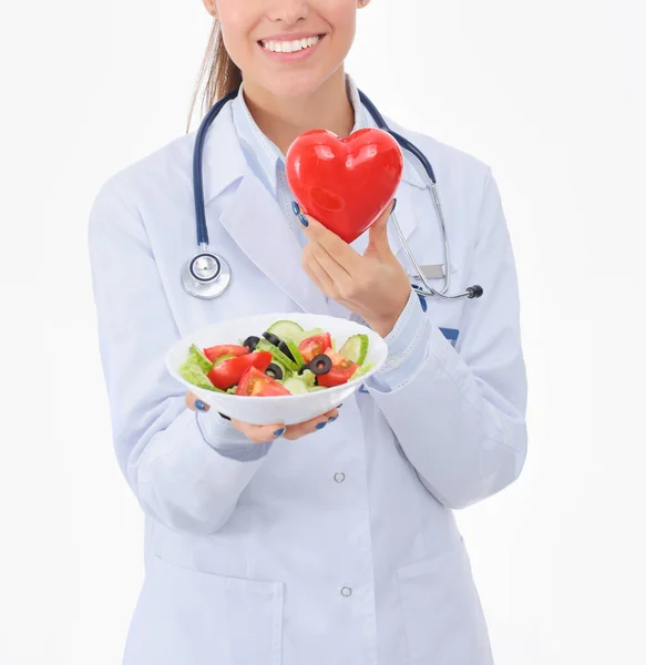 Retrato de una hermosa doctora sosteniendo un plato con vegetales frescos y corazón rojo. Mujeres doctores . — Foto de Stock