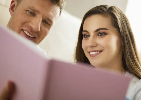 Nettes Paar beim Auspacken von Kartons in seinem neuen Zuhause, auf dem Boden sitzend und ein Familienalbum anschauend — Stockfoto