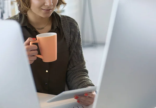 Mulher atraente sentado na mesa do escritório, segurando uma xícara de café — Fotografia de Stock