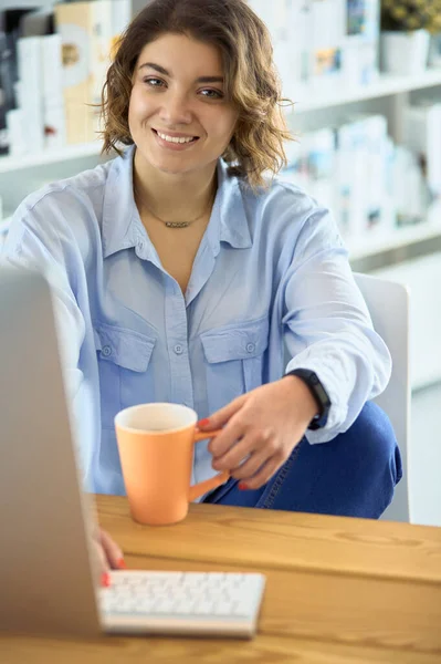 O femeie atractivă stând la birou, ţinând o ceaşcă de cafea — Fotografie, imagine de stoc