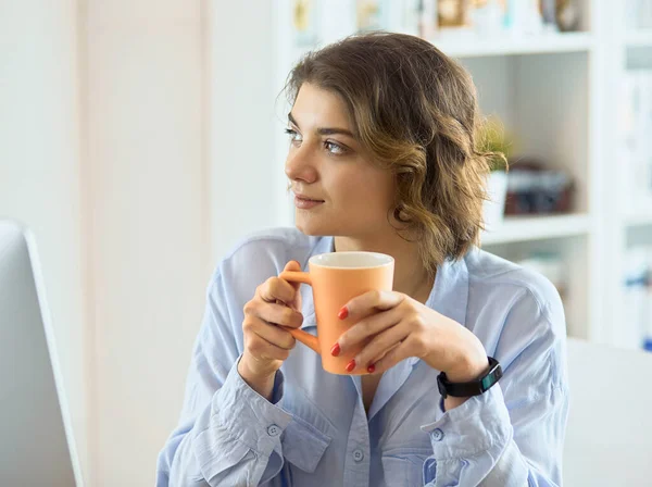 Donna attraente seduta alla scrivania dell'ufficio, con in mano una tazza di caffè — Foto Stock