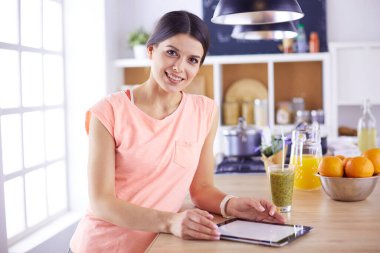 Mutfakta dijital tablet kullanan güzel genç bir kadın.