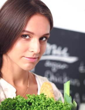 Mutfakta elinde sebzelerle gülümseyen genç bir kadın. Gülümseyen genç kadın