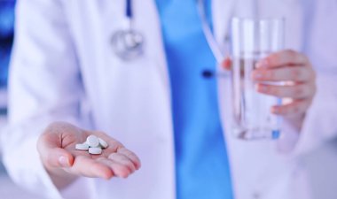 Doktorların ellerinde haplar ve bir bardak su tutarken yakın plan çekimleri..
