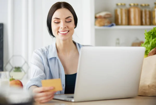キッチンでコンピュータやクレジットカードを使用して笑顔の女性オンラインショッピング — ストック写真