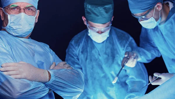 Grupo de cirurgiões no trabalho em sala de operações tonificada em azul. Equipe médica realizando operação — Fotografia de Stock