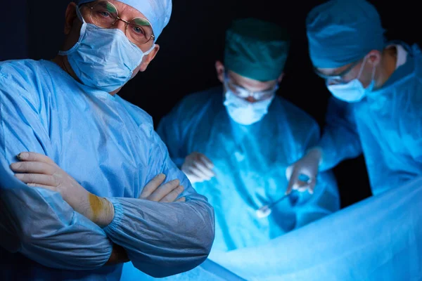 Grupo de cirurgiões no trabalho em sala de operações tonificada em azul. Equipe médica realizando operação — Fotografia de Stock