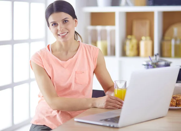 Ung kvinna i köket med bärbar dator ser recept, leende. Begreppet livsmedelsbloggare — Stockfoto
