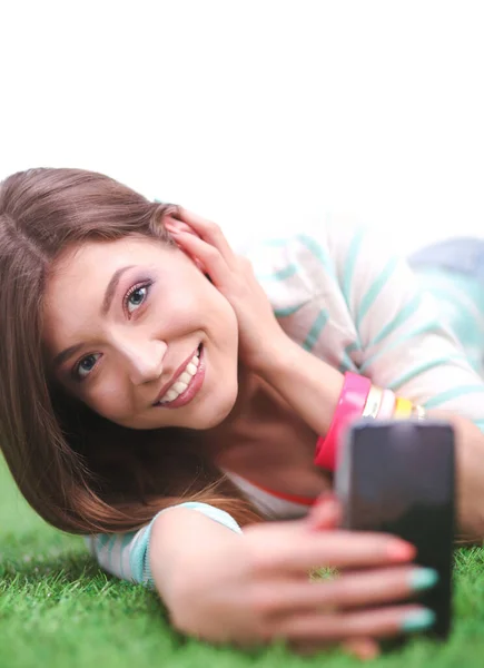 Schöne junge Frau macht Selfie mit ihrem Handy, während sie im grünen Gras liegt. Schöne junge Frau macht Selfie — Stockfoto