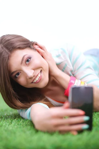 Schöne junge Frau macht Selfie mit ihrem Handy, während sie im grünen Gras liegt. Schöne junge Frau macht Selfie — Stockfoto