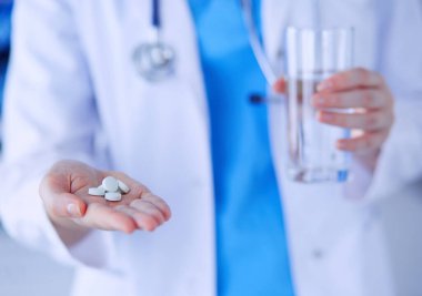 Doktorların ellerinde haplar ve bir bardak su tutarken yakın plan çekimleri..