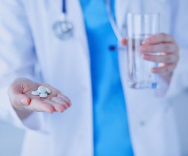 Doktorların ellerinde haplar ve bir bardak su tutarken yakın plan çekimleri..