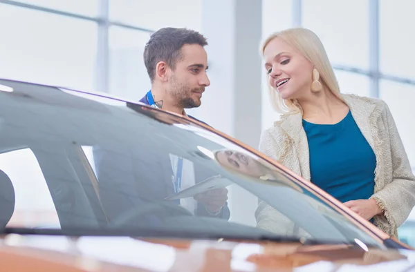 Obchodník se ženou stojí v blízkosti nového auta v showroomu — Stock fotografie