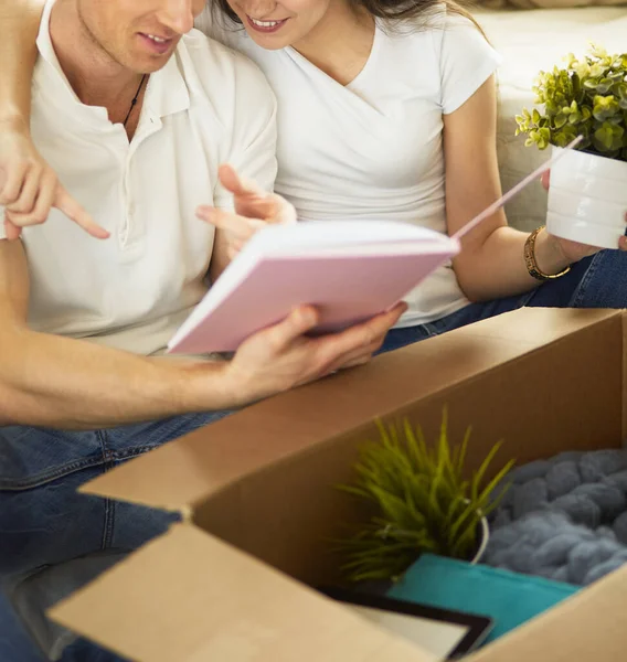 Nettes Paar beim Auspacken von Kartons in seinem neuen Zuhause, auf dem Boden sitzend und ein Familienalbum anschauend — Stockfoto