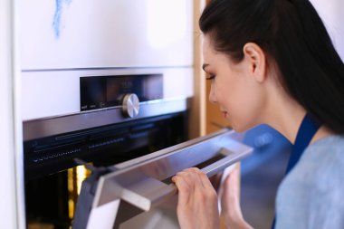 Güzel genç bayan pastasının fırında ne yaptığını kontrol ediyor.