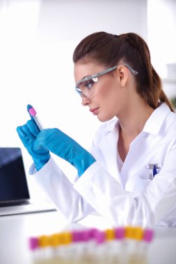 Kadın araştırmacı, beyaz arka planda izole edilmiş ilaç şişeleri ve mataralarla çevrili.