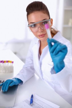 Kadın araştırmacı, beyaz arka planda izole edilmiş ilaç şişeleri ve mataralarla çevrili.