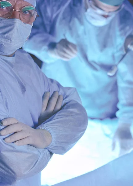 Group of surgeons at work in operating theater toned in blue. Medical team performing operation — Stock Photo, Image