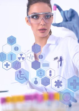 Kadın araştırmacı, beyaz arka planda izole edilmiş ilaç şişeleri ve mataralarla çevrili.