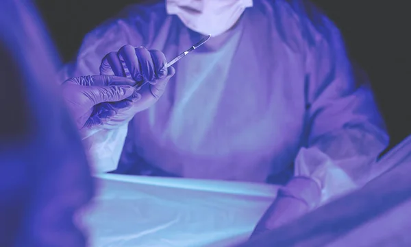 Médico realizando cirurgia em um fundo escuro. — Fotografia de Stock