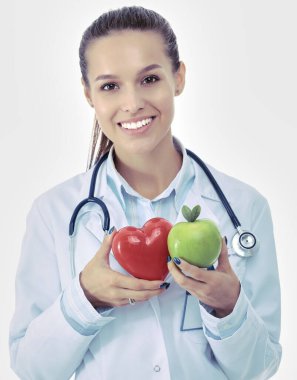 Güzel gülümseyen kadın doktor elinde kırmızı kalp ve yeşil elma tutuyor.