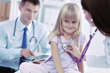 Kadın doktor ameliyatta steteskopla çocuğu muayene ediyor.