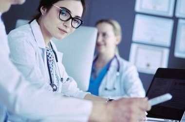 Ciddi bir tıbbi ekip parlak bir ofiste dizüstü bilgisayar kullanıyor.