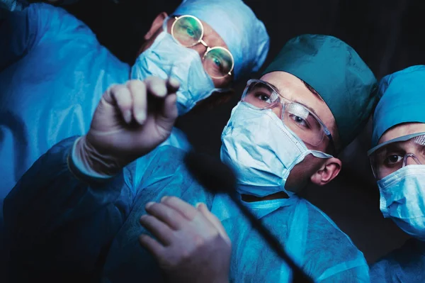 Группа хирургов за работой в операционной тонизирована в синий цвет. Медицинская команда, выполняющая операцию — стоковое фото