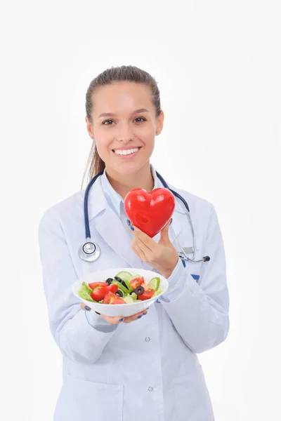 Portrait of a beautiful woman doctor holding a plate with fresh vegetables and red heart. Woman doctors. — Stock Photo, Image