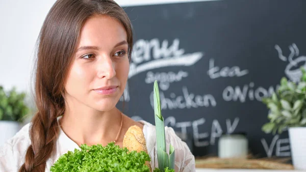 Mutfakta elinde sebzelerle gülümseyen genç bir kadın. Gülümseyen genç kadın