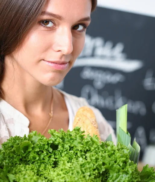 Mujer joven sonriente sosteniendo verduras de pie en la cocina. Jovencita sonriente — Foto de Stock