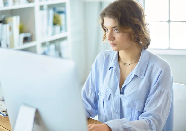 Jolie jeune femme assise au bureau et tapant sur un ordinateur portable — Photo