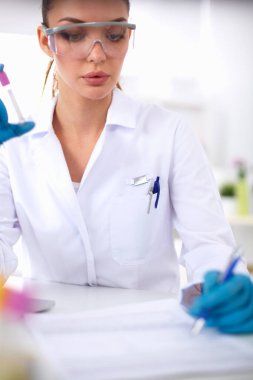 Kadın araştırmacı, beyaz arka planda izole edilmiş ilaç şişeleri ve mataralarla çevrili.